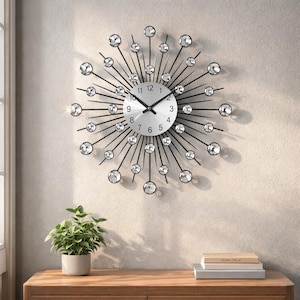 May include: A decorative wall clock with a silver face and black hands. The clock features a starburst design with black rods and clear crystal accents. The clock is mounted on a light-colored wall.