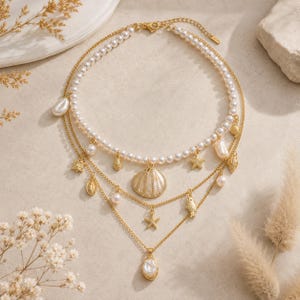 Peut inclure: Ensemble de colliers superposés à trois rangs. Le rang supérieur est un collier de perles, les deuxième et troisième rangs sont des chaînes dorées avec des breloques coquillage, étoile de mer et perle. Le collier a un fermoir doré.