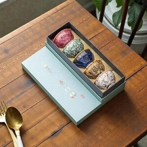 Peut inclure: Un ensemble de cinq tasses à thé en céramique dans une boîte rectangulaire. Les tasses sont dans les tons de rouge, vert, bleu, marron et blanc. La boîte est bleu clair avec du texte doré et un tampon rouge.