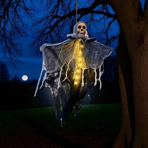 Peut inclure: Décoration d'Halloween suspendue représentant un squelette lumineux avec une cape noire et grise déchirée. La tête du squelette est éclairée et la cape a un design déchiré. L'arrière-plan est un ciel nocturne bleu foncé avec une pleine lune.