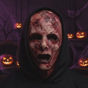 May include: A full-head latex mask featuring a realistic, textured, and bloodied skin appearance with deep red lacerations, dark bruising, and an open mouth expression. The mask is worn with a plain black hooded sweatshirt that covers the head and neck.
