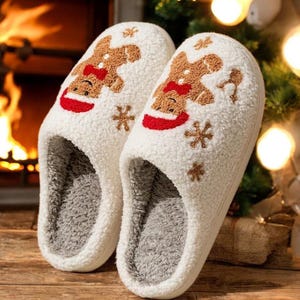 Peut inclure: Une paire de pantoufles blanches et moelleuses avec un motif de bonhomme en pain d'épices. Les pantoufles ont un nœud papillon et un chapeau rouges, avec des flocons de neige brodés. L'intérieur est gris doux, parfait pour l'intérieur.
