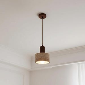 Peut inclure: Un luminaire suspendu moderne avec un abat-jour cylindrique beige texturé et un dessus et une base marron foncé. La lumière est suspendue à un cordon marron et est fixée au plafond avec un luminaire marron assorti.