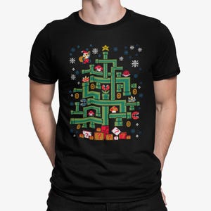 May include: Black t-shirt featuring a pixelated Christmas tree design inspired by the Super Mario Bros. video game. The tree is composed of green pipes, with characters and elements from the game, and snowflakes. A star tops the tree.