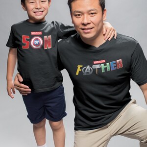 May include: A father and son wearing matching black t-shirts with the words "Marvelous Son" and "Marvelous Father" printed on them. The shirts feature various Marvel superhero logos and symbols.
