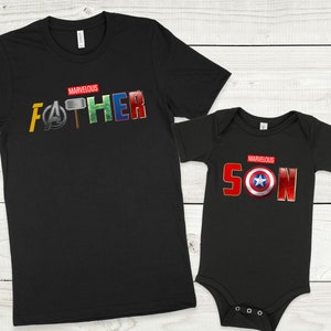 May include: Black t-shirts with the words "MARVELOUS FATHER" and "MARVELOUS SON" in red letters. The letters are decorated with superhero logos and symbols from the Marvel universe.