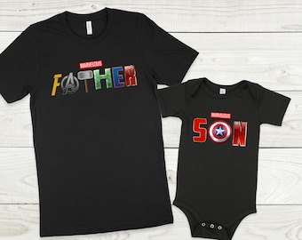 May include: Black t-shirts with the words "MARVELOUS FATHER" and "MARVELOUS SON" in red letters. The letters are decorated with superhero logos and symbols from the Marvel universe.