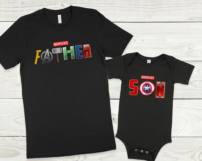 May include: Black t-shirts with the words "MARVELOUS FATHER" and "MARVELOUS SON" in red letters. The letters are decorated with superhero logos and symbols from the Marvel universe.