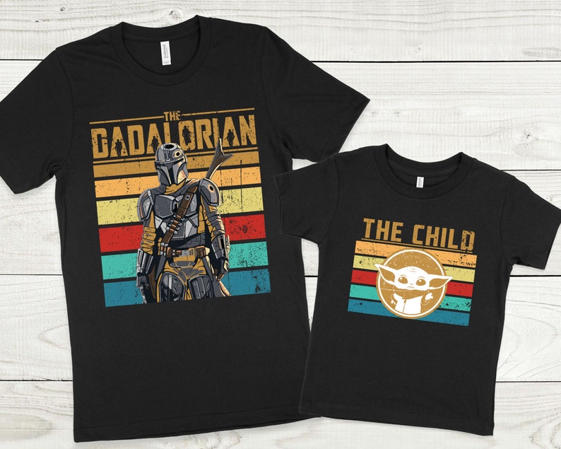 May include: Two black t-shirts with a retro design. The larger shirt features a character from Star Wars: The Mandalorian, with the text "The  Dadalorian". The smaller shirt features a character from Star Wars: The Mandalorian, with the text "The Child".