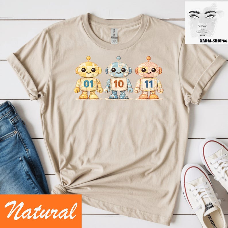 May include: Beige t-shirt with three cartoon robots, each with a different number: 01, 10, and 11. The robots are yellow, blue, and orange with stitched details. The word "Natural" is printed on the bottom left.