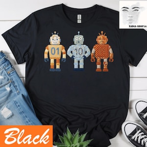 Könnte beinhalten: Schwarzes T-Shirt mit drei bunten Roboter-Designs. Jeder Roboter hat ein einzigartiges Muster und eine Nummer: 01, 10 und ein weiterer Roboter. Die Roboter sind in Orange-, Blau- und Brauntönen gehalten. Das Wort "Black" befindet sich in einer orangefarbenen Box unten links.