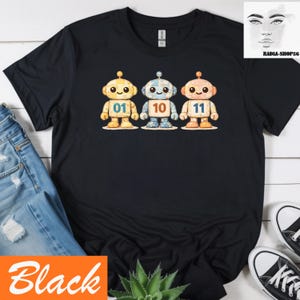 May include: Black t-shirt with three cartoon robots, each with a different number: 01, 10, and 11. The robots are in yellow, blue, and orange. The word "Black" is in an orange box at the bottom of the image.