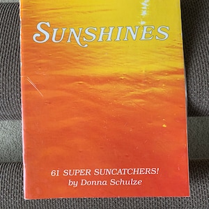 May include: A book titled "SUNSHINES" with a yellow and orange background. The book cover features the text "61 SUPER SUNCATCHERS! by Donna Schulze".