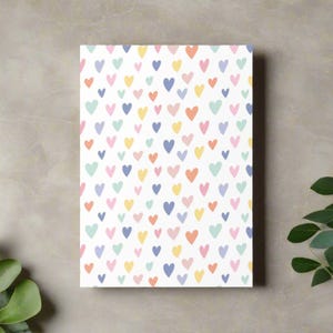 May include: A rectangular white canvas covered in a pattern of small, colorful hearts. The hearts are in shades of blue, yellow, pink, orange, and green. The background is a neutral gray.