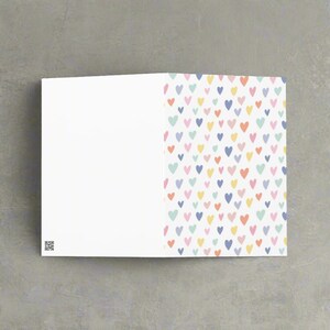 May include: A folded greeting card with a white interior and a colorful heart pattern on the right side. The hearts are in various pastel colors, including pink, yellow, blue, and green. A QR code is in the lower left corner.