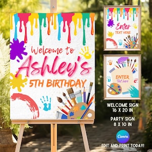 Pode incluir: Um cavalete de madeira exibe uma placa de boas-vindas para o 5º aniversário de Ashley. A placa apresenta gotas de tinta coloridas, respingos, impressões de mãos e materiais de arte. Duas placas emolduradas também são visíveis. A placa de boas-vindas tem 40.6 x 50.8 cm.