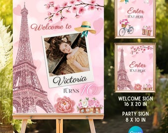 May include: A pink welcome sign featuring a large Eiffel Tower illustration, cherry blossom branches, a straw hat, and a central photo frame with the text Welcome to Victoria Turns 10. Includes smaller 40.6x50.8 cm and 20.3x25.4 cm sign templates.