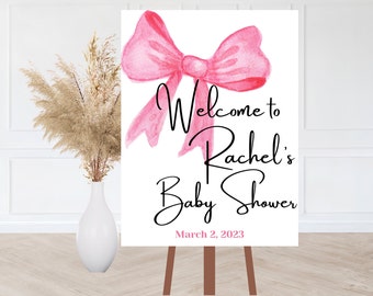May include: A white sign with a pink bow and black text that reads "Welcome to Rachel's Baby Shower March 2, 2023".