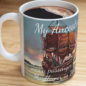 May include: White ceramic mug filled with dark coffee. The mug features a vintage illustration of a tall ship with brown sails and the text "My Ancestor was a passenger on the Mayflower in 1620."