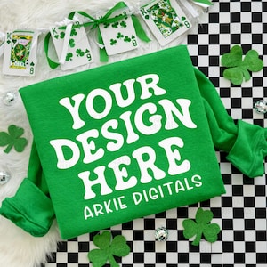 May include: A green sweatshirt with the text "YOUR DESIGN HERE" and "ARKIE DIGITALS" in white. The image includes playing cards with shamrocks, green shamrock cutouts, and disco balls, all on a black and white checkered surface.