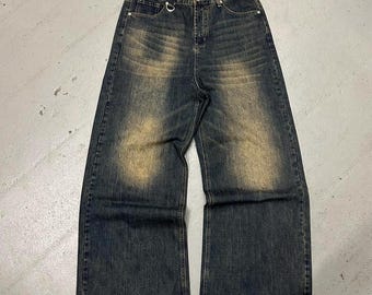 May include: Dark wash denim jeans with a wide leg design. The jeans have a faded, distressed appearance with lighter patches on the front. Features include a metal ring detail on the front and classic five-pocket styling.