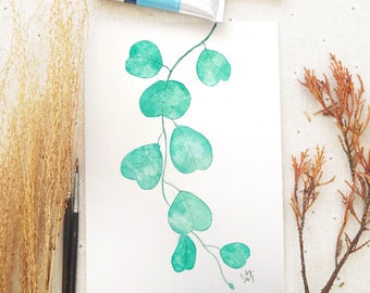 May include: Watercolor painting of a green eucalyptus branch with leaves. The painting is on white paper and has a signature in the bottom right corner.