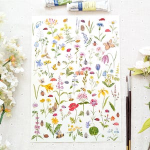 Puede incluir: Acuarela de varias flores silvestres, insectos y mariposas en tonos amarillos, rosas, azules y naranjas. Se ven dos pinceles y tubos de pintura. La obra de arte está sobre un fondo blanco.