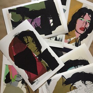 May include: A collection of overlapping art prints featuring stylized portraits and abstract geometric shapes in black, olive green, mustard yellow, pink, and red. Each print displays bold ink lines, layered color blocks, and a signature at the bottom.