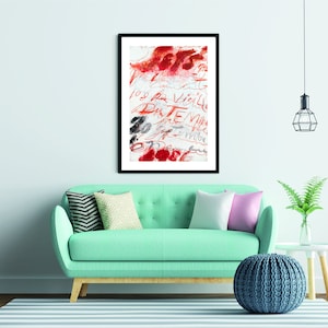 May include: A framed abstract art print with red and black brushstrokes and handwritten text in French. The print is hanging on a light blue wall above a teal sofa with pillows and a blue knitted pouf.
