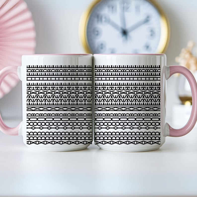 Pode incluir: Duas canecas de cer&acirc;mica brancas com al&ccedil;as e bordas rosa. Cada caneca apresenta um padr&atilde;o geom&eacute;trico preto de linhas e formas horizontais. Um rel&oacute;gio com moldura dourada &eacute; vis&iacute;vel ao fundo.