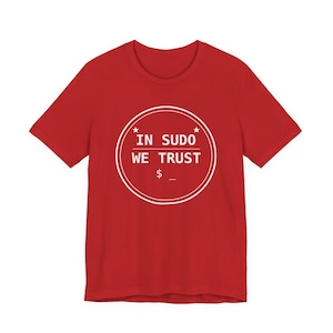May include: A red short-sleeved t-shirt featuring a white circular graphic on the chest. The graphic contains the text IN SUDO WE TRUST, a dollar sign, an underscore, and two small stars, all enclosed within a double-lined white circle.