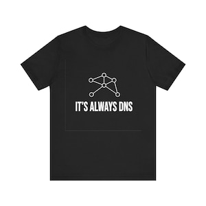 May include: A black short-sleeved t-shirt featuring a white graphic of a network node diagram above the text IT'S ALWAYS DNS. The design is centered on the chest of the shirt, which has a crew neckline and a standard fit for casual wear.