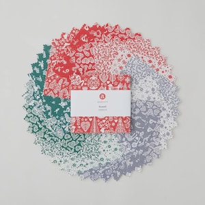 May include: A circular arrangement of fabric squares in shades of red, green, and gray, each patterned with white holiday-themed designs. A rectangular card with the word "andover" and "Seandi" is centered.