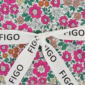 May include: A floral fabric square with a white ribbon tied around it. The fabric features a pattern of pink, orange, and yellow flowers on a white background. The ribbon has the word "FIGO" printed on it in black.