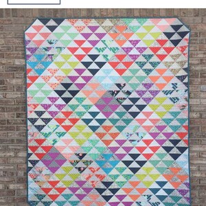 May include: A colorful quilt with a geometric triangle pattern. The quilt features a variety of colors including red, orange, yellow, green, blue, purple, and black. The quilt is displayed against a brick wall. The text "Triangle Parade" is visible.