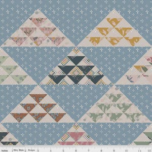 May include: A fabric pattern featuring repeating triangle shapes in various colors and patterns, including floral and geometric designs. The triangles are set against a light blue background with small white cross-shaped accents. The text "Inches" and "Riley Blake Designs" is visible.
