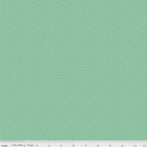 May include: A light green fabric with a repeating pattern of small, white and blue floral shapes. The fabric is marked with inches along the bottom edge, with the text "Riley Blake Designs" visible.