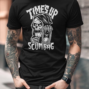 May include: Black t-shirt with a white graphic of a grim reaper holding an hourglass. The text "TIMES UP SCUMBAG" is above and below the graphic. The shirt is a crew neck style.