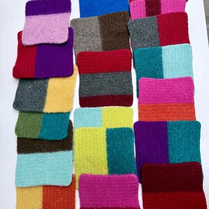 May include: A collection of colorful, rectangular, knitted coasters. Each coaster features two or three blocks of color, including shades of pink, purple, red, blue, green, yellow, and brown. The coasters are arranged on a white surface.