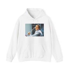 Puede incluir: Sudadera con capucha blanca con bolsillo delantero y cordón. La sudadera presenta una imagen rectangular de un hombre sosteniendo un arma. El hombre está sonriendo. La imagen es de la película American Psycho.