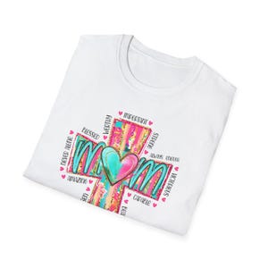 Könnte beinhalten: Weißes T-Shirt mit einem farbenfrohen Kreuzdesign. Das Design zeigt das Wort "Mom" in Türkis, ein Herz und umgebende Wörter wie "Blessed" und "Important". Kleine rosa Herzen sind um das Design verstreut.