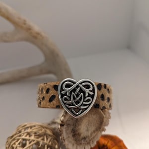 May include: A brown and black leopard print bracelet with a silver heart-shaped charm. The charm has a Celtic knot design.