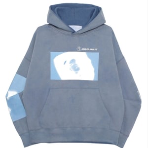 Peut inclure: Un sweat à capuche bleu-gris avec une poche avant et une capuche. Le sweat à capuche présente un motif carré bleu clair avec un visage et le texte "JUNGLES JUNGLES". Les manches ont des motifs bleu clair et bleu-gris.