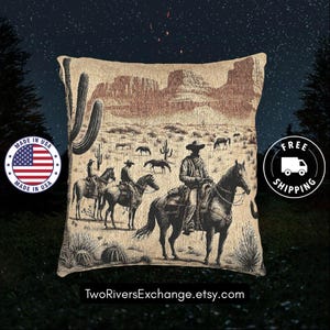 May include: Beige tapestry pillow featuring a Western scene with cowboys on horseback, cacti, and a desert landscape. The pillow has a vintage aesthetic, with a detailed illustration in shades of brown and black. The pillow is square-shaped.