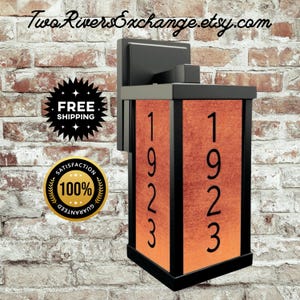 Puede incluir: Luminaria de pared exterior negra con los números 1923 en negro sobre un fondo naranja. La luminaria es rectangular y tiene un marco negro. El nombre de la tienda Etsy es visible en la parte superior.