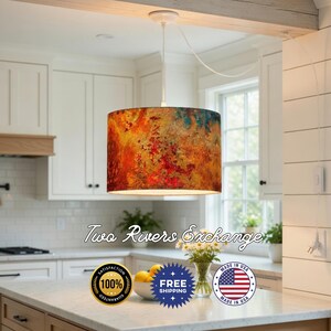 May include: A cylindrical pendant lamp with a colorful abstract design in shades of orange, red, and blue. The lamp hangs from a white cord and is suspended in a kitchen setting. The text "Two Rivers Exchange" is visible on the image.