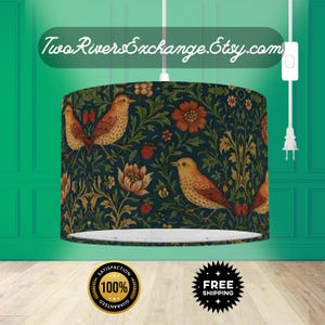 May include: A drum lampshade with a dark blue floral and bird pattern in orange, brown, and green. The text "Two Rivers Exchange.Etsy.com" is visible on the top. The lampshade is suspended from a white cord. The design includes flowers, birds, and foliage.