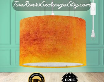 May include: A cylindrical lampshade with a textured, abstract design in shades of orange and yellow. The lampshade is suspended from the ceiling by a white cord. The text "Two Rivers Exchange.Etsy.com" is visible on the top.