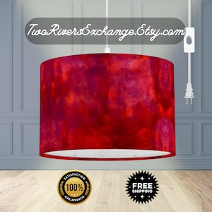 May include: A cylindrical lampshade with a vibrant abstract design in shades of red, pink, and orange. The lampshade is suspended from a white cord and features the text "Two Rivers Exchange.Etsy.com".