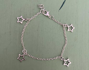 May include: Silver-toned chain bracelet featuring five open star charms. The bracelet has a lobster clasp closure and is designed for wrist wear. The stars are evenly spaced along the chain, creating a celestial theme. A delicate piece of jewelry.